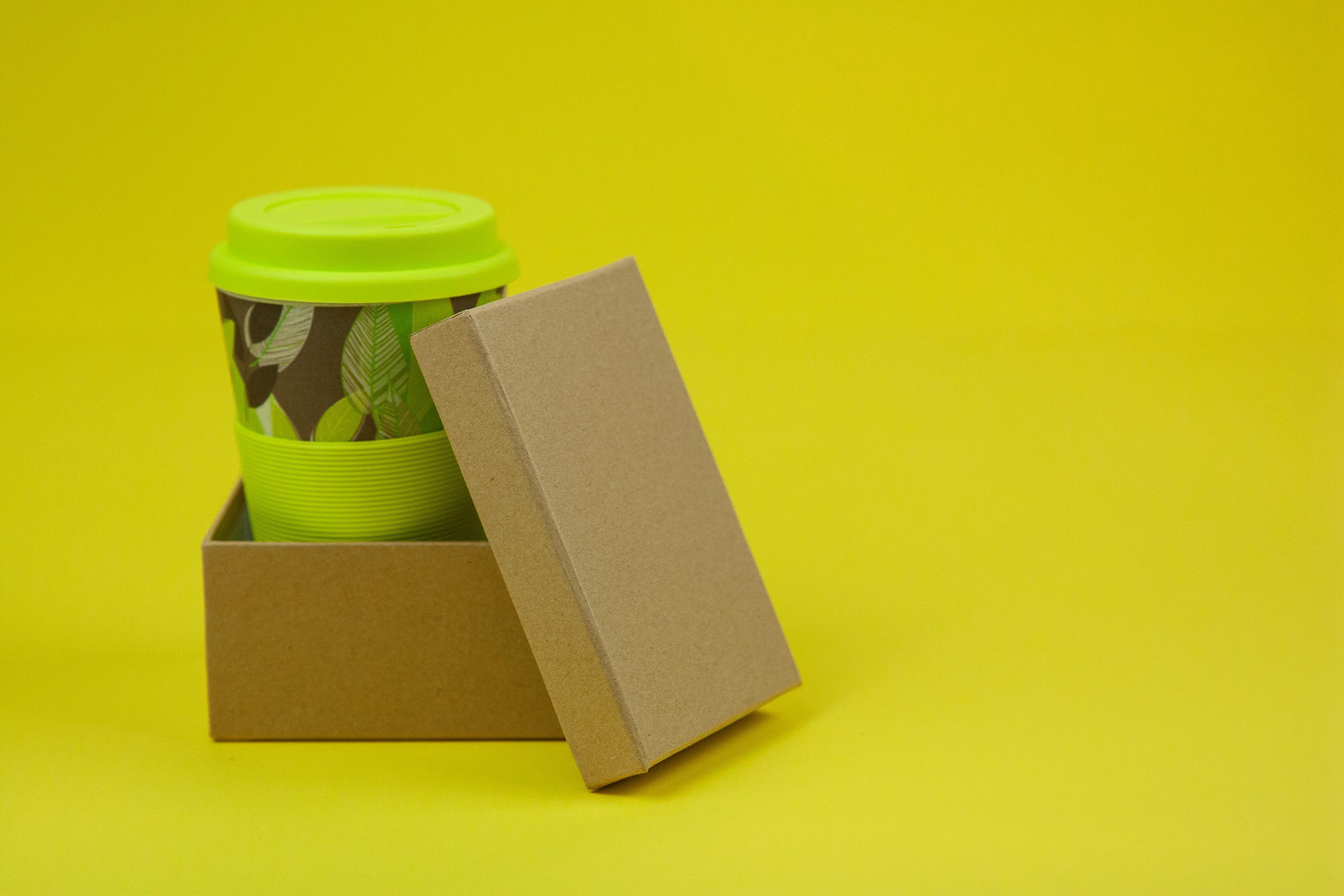 Green coffee cup inside cardboard box with yellow background